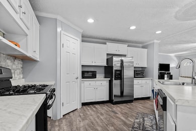Kitchen with black appliances, a textured ceiling, wood finished floors, ornamental molding, and white cabinetry