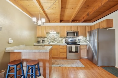 Kitchen with appliances with stainless steel finishes, a wooden ceiling with exposed beams, backsplash, a peninsula, and light countertops