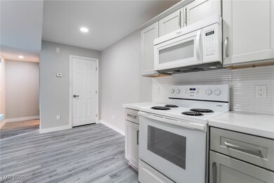 Kitchen with light hardwood / wood-style floors, white appliances, tasteful backsplash, light stone counters, and white cabinets