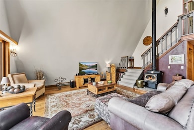 Living room featuring stairway, high vaulted ceiling, wood finished floors, a wood stove, and baseboard heating