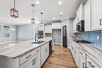 Kitchen featuring an island with sink, crown molding, light stone countertops, white cabinets, and decorative light fixtures.