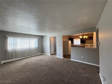 Unfurnished room featuring dark colored carpet, a baseboard radiator, a textured ceiling, and a notable chandelier