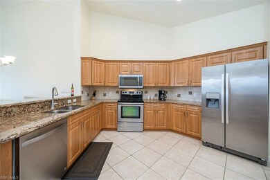 Kitchen with appliances with stainless steel finishes, light stone counters, high vaulted ceiling, light tile patterned floors, and decorative backsplash