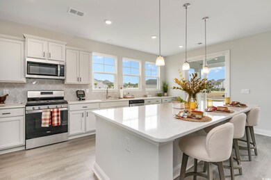 Kitchen featuring appliances with stainless steel finishes, light wood-type flooring, decorative backsplash, a kitchen island, and light countertops