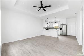 Unfurnished living room with a tray ceiling, wood finished floors, and a ceiling fan