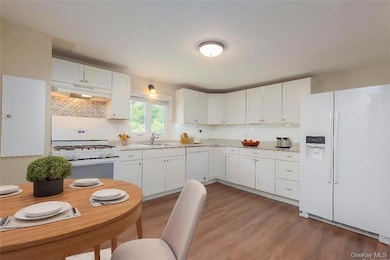 Kitchen featuring white cabinetry, hardwood / wood-style flooring, sink, and white appliances