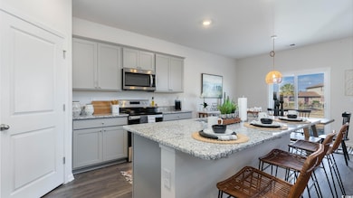 Virtually staged Kitchen with stainless steel appliances, gray cabinets, a kitchen breakfast bar, dark wood-style flooring, and light stone counters