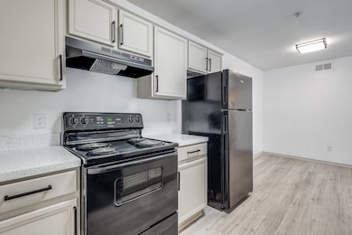 Kitchen featuring under cabinet range hood, visible vents, black appliances, and light wood-style flooring