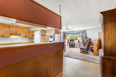 Kitchen featuring light floors, ceiling fan, light countertops, brown cabinetry, and freestanding refrigerator