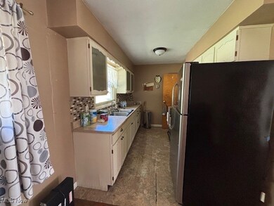 Kitchen with freestanding refrigerator, light countertops, white cabinets, and backsplash