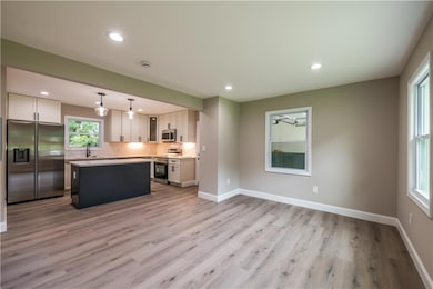 Kitchen featuring stainless steel appliances, a center island, light wood-type flooring, light countertops, and backsplash