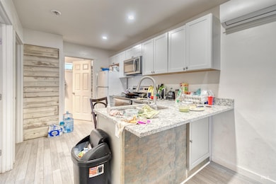 Kitchen with stainless steel appliances, a wall mounted AC, light wood-style floors, a breakfast bar area, and light stone countertops