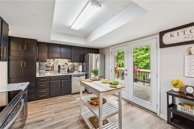 Kitchen with stainless steel appliances, a tray ceiling, a sink, light wood-style floors, and backsplash