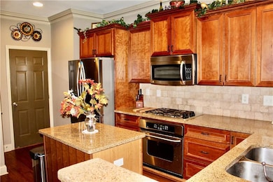 Kitchen featuring appliances with stainless steel finishes, light stone counters, backsplash, a center island, and ornamental molding