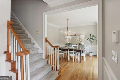 Dining space featuring ornamental molding, light wood-type flooring, stairs, a chandelier, and wainscoting