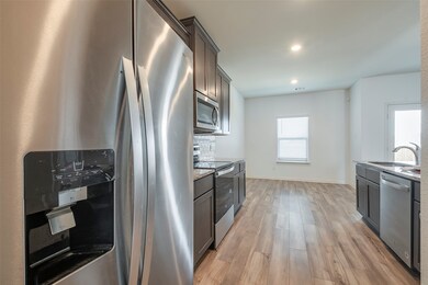 Kitchen featuring backsplash, sink, light stone countertops, appliances with stainless steel finishes, and light hardwood / wood-style flooring