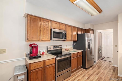 Kitchen featuring appliances with stainless steel finishes, light countertops, brown cabinets, and light wood-type flooring