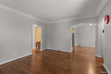 Unfurnished room featuring arched walkways, ornamental molding, dark wood finished floors, and a textured ceiling