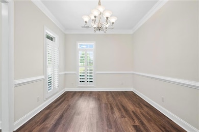 Spare room with a chandelier, dark wood-style flooring, and ornamental molding