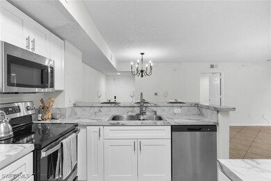 Kitchen featuring appliances with stainless steel finishes, white cabinetry, a chandelier, light tile patterned floors, and a peninsula