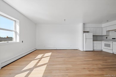 Kitchen featuring white appliances, baseboard heating, light wood-style flooring, decorative backsplash, and white cabinets