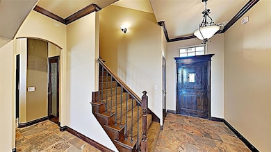 Foyer with stone tile floors, ornamental molding, and stairs