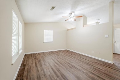Empty room with a ceiling fan, plenty of natural light, wood finished floors, a textured ceiling, and vaulted ceiling