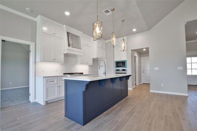 Kitchen with decorative light fixtures, a kitchen island with sink, black microwave, stainless steel oven, and white cabinets