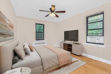 Bedroom with light wood-type flooring, ceiling fan, radiator heating unit, and cooling unit