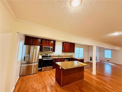 Kitchen with crown molding, appliances with stainless steel finishes, a textured ceiling, light stone countertops, and light wood-style flooring