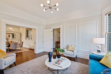 Large formal living room with bay window, gas fireplace with stone surround and decorative moldings, hardwood floors, and period pocket doors opening to the dining room