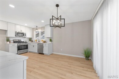 Kitchen featuring appliances with stainless steel finishes, white cabinets, decorative backsplash, light wood-type flooring, and pendant lighting