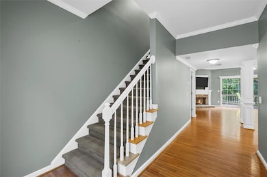 Stairs featuring ornamental molding, wood finished floors, a fireplace, and decorative columns