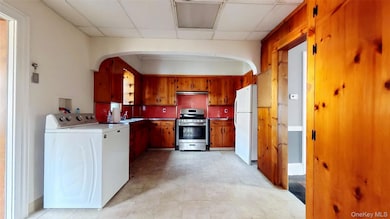 Kitchen with washer / clothes dryer, a drop ceiling, stainless steel gas stove, brown cabinets, and freestanding refrigerator