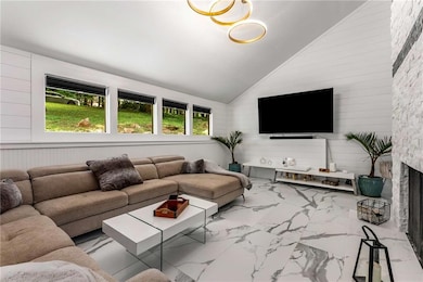 Living room featuring wooden walls, a fireplace, light tile patterned floors, and high vaulted ceiling