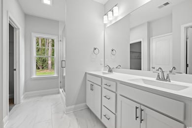 Bathroom with double vanity, light marble finish floors, and a stall shower