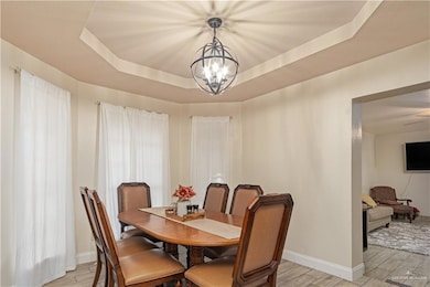 Dining area with a raised ceiling, a chandelier, wood finish floors, and baseboards