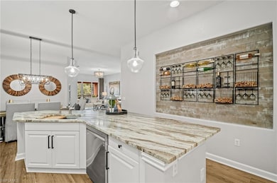 Kitchen featuring stainless steel dishwasher, a chandelier, white cabinets, and light stone counters