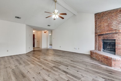 Unfurnished living room with a brick fireplace, light wood-type flooring, beamed ceiling, high vaulted ceiling, and ceiling fan