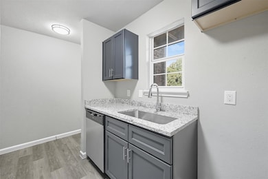 Kitchen featuring light stone counters, stainless steel dishwasher, light wood-type flooring, and gray cabinets