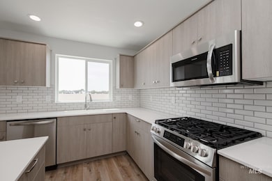 Kitchen with light brown cabinetry, stainless steel appliances, light wood finished floors, light stone counters, and recessed lighting