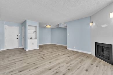 Unfurnished living room with a textured ceiling, light wood-style flooring, and a large fireplace