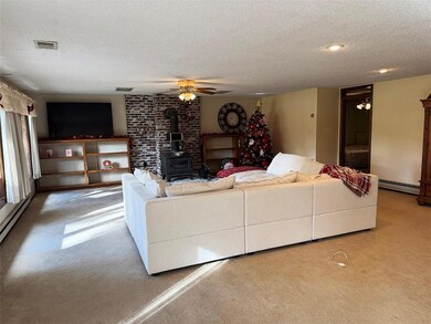 Living area with a wood stove, a textured ceiling, a ceiling fan, carpet, and baseboard heating
