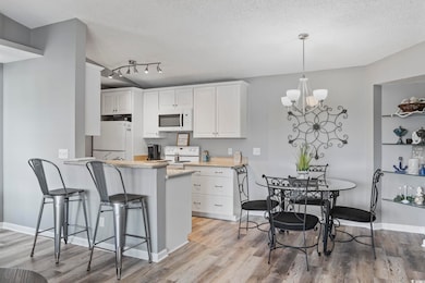 Kitchen with white appliances, light wood-style floors, white cabinetry, a textured ceiling, and a peninsula