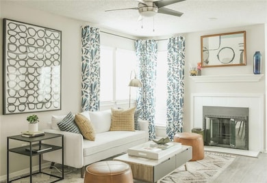 Living area featuring a tile fireplace, a textured ceiling, ceiling fan, and light hardwood / wood-style floors