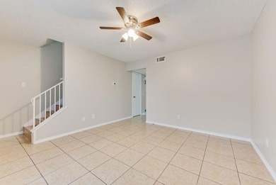 Empty room with a textured ceiling, light tile patterned floors, a ceiling fan, and stairs