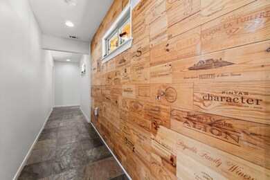 This hallway features a unique accent wall made of wine crate panels, adding character and warmth. It has a slate tile floor and recessed lighting, giving it a modern and inviting feel.