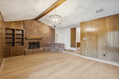 Living room featuring wood walls, light wood-style flooring, a textured ceiling, a brick fireplace, and a chandelier