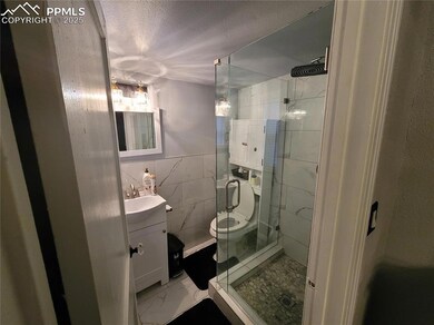 Unit 1 Bathroom featuring vanity, a stall shower, a textured ceiling, toilet, and marble look tiles
