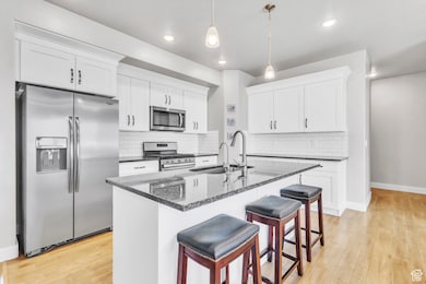 Kitchen with stainless steel appliances, a breakfast bar, decorative backsplash, white cabinetry, and pendant lighting